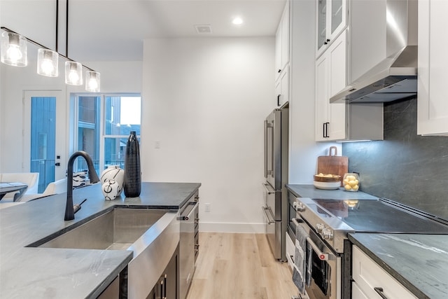 kitchen with white cabinets, appliances with stainless steel finishes, and wall chimney range hood