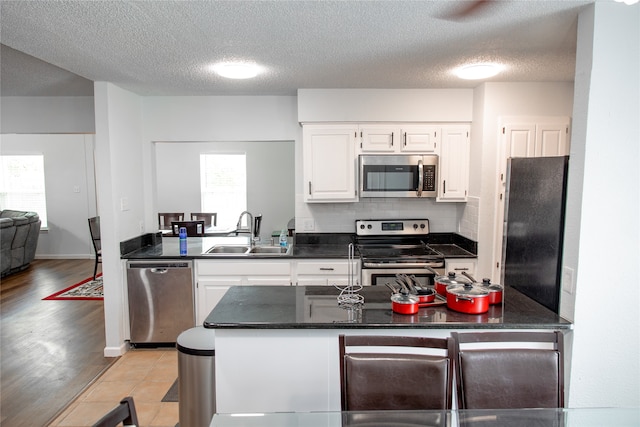 kitchen with sink, white cabinets, kitchen peninsula, light hardwood / wood-style flooring, and appliances with stainless steel finishes