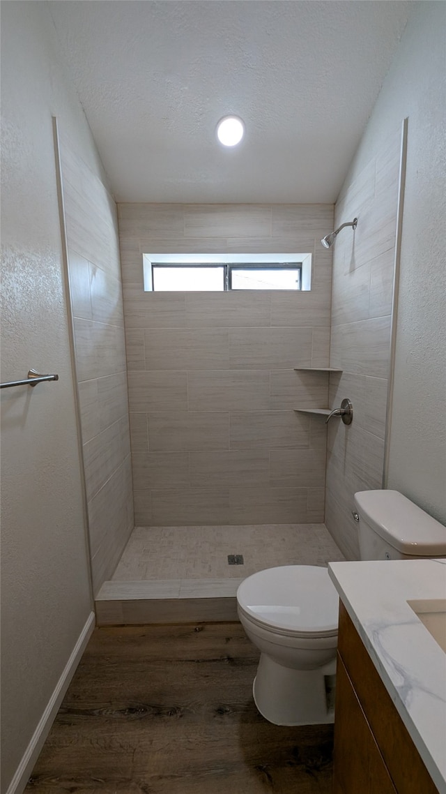 bathroom with wood-type flooring, vanity, a tile shower, and toilet