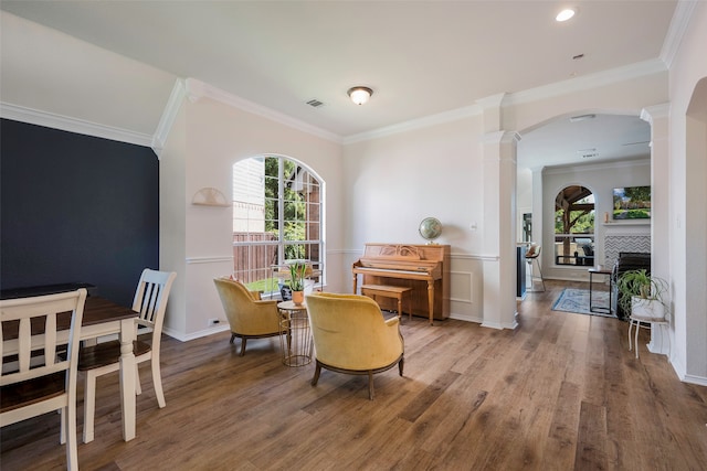 dining space featuring wood-type flooring, decorative columns, ornamental molding, and a tiled fireplace