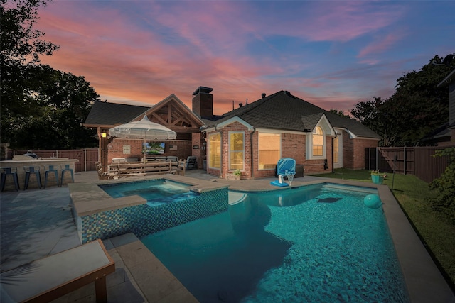 pool at dusk with a patio area, an outdoor bar, and an in ground hot tub