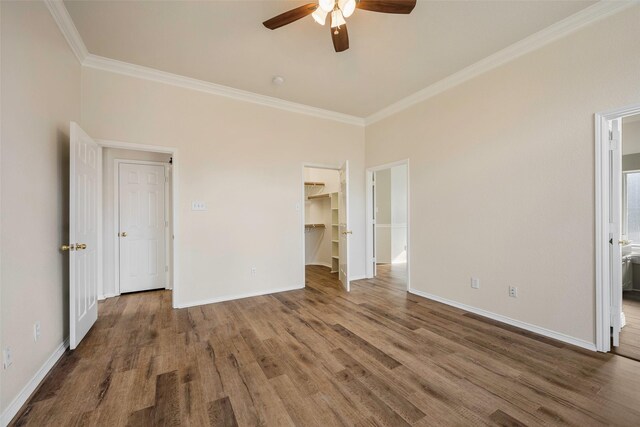 unfurnished bedroom featuring ceiling fan, a spacious closet, crown molding, hardwood / wood-style floors, and a closet