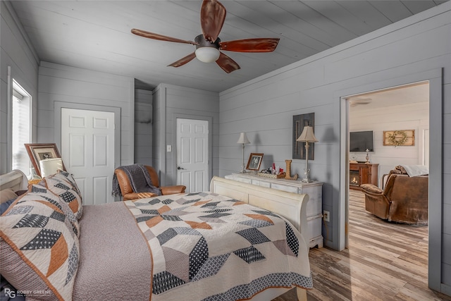 bedroom with ceiling fan, light hardwood / wood-style flooring, and wood walls