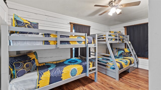 bedroom with wood-type flooring, wood walls, and ceiling fan