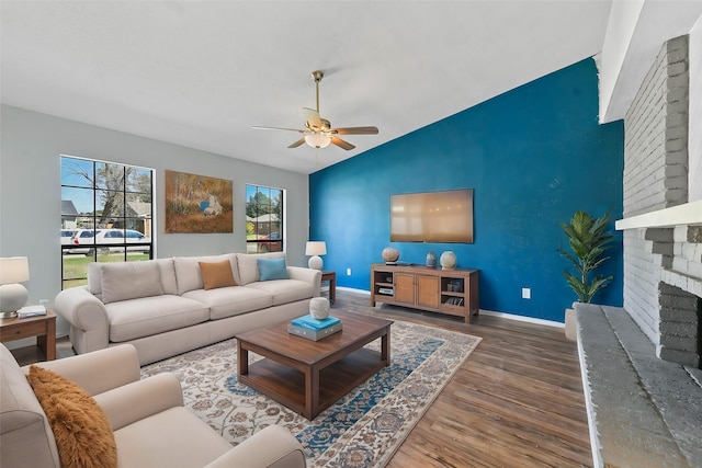 living room featuring dark wood-type flooring, ceiling fan, a fireplace, and vaulted ceiling