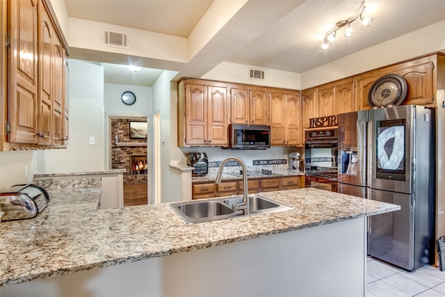 kitchen featuring sink, kitchen peninsula, appliances with stainless steel finishes, light tile patterned floors, and light stone countertops