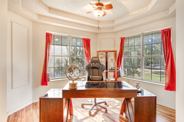 office area featuring light wood-type flooring, a raised ceiling, a textured ceiling, and ceiling fan