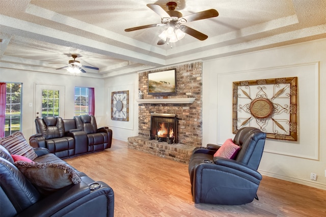 living room featuring a raised ceiling, a fireplace, wood-type flooring, and ceiling fan