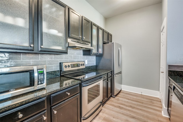 kitchen with appliances with stainless steel finishes, light hardwood / wood-style floors, dark stone counters, and tasteful backsplash