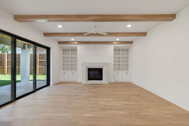 unfurnished living room with ceiling fan, beamed ceiling, light wood-type flooring, and built in shelves