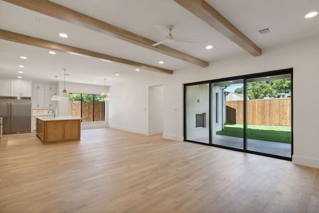 unfurnished living room featuring ceiling fan with notable chandelier, light wood-type flooring, and beam ceiling