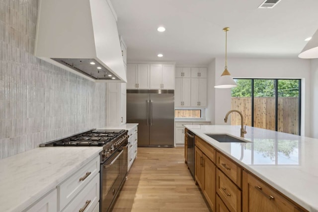 kitchen featuring hanging light fixtures, sink, white cabinetry, light stone countertops, and high quality appliances