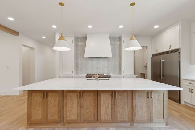 kitchen featuring pendant lighting, premium range hood, a large island with sink, and white cabinetry