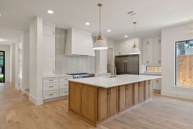 kitchen featuring custom range hood, a large island with sink, white cabinetry, and stainless steel appliances