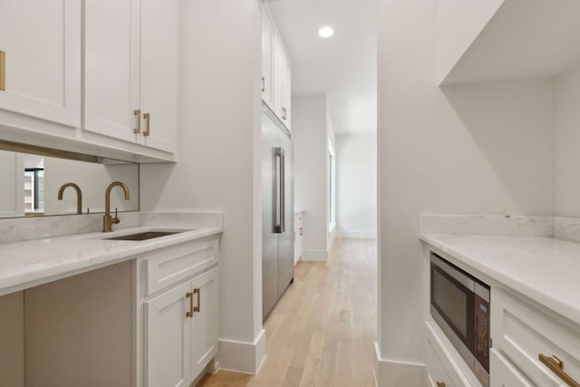 kitchen featuring light wood-type flooring, light stone counters, sink, white cabinetry, and stainless steel microwave