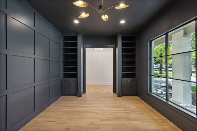 spacious closet with light wood-type flooring and a notable chandelier