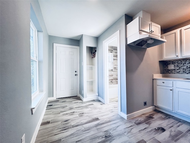 kitchen featuring white cabinets, backsplash, light wood-type flooring, and extractor fan