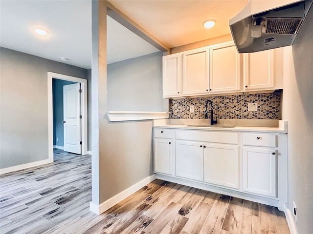 kitchen with sink, range hood, white cabinets, decorative backsplash, and light hardwood / wood-style flooring