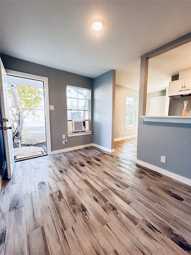 unfurnished living room featuring cooling unit, a textured ceiling, light hardwood / wood-style floors, and a wall unit AC