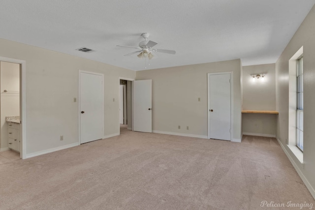 unfurnished bedroom featuring light carpet, connected bathroom, and ceiling fan