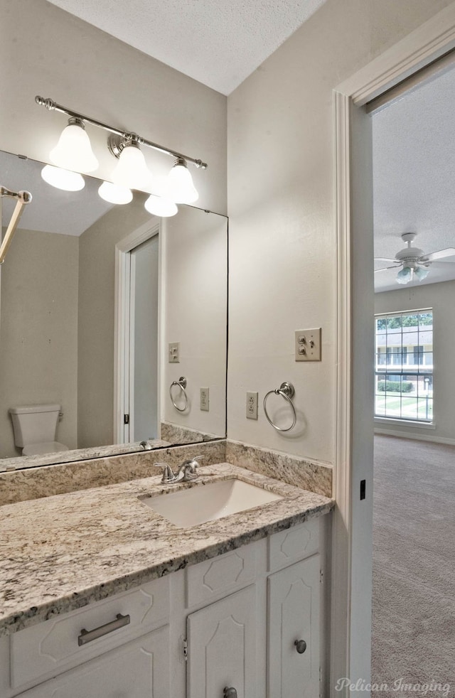 bathroom with ceiling fan, vanity, toilet, and a textured ceiling