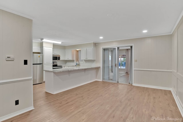 kitchen with appliances with stainless steel finishes, light hardwood / wood-style floors, light stone counters, white cabinets, and kitchen peninsula