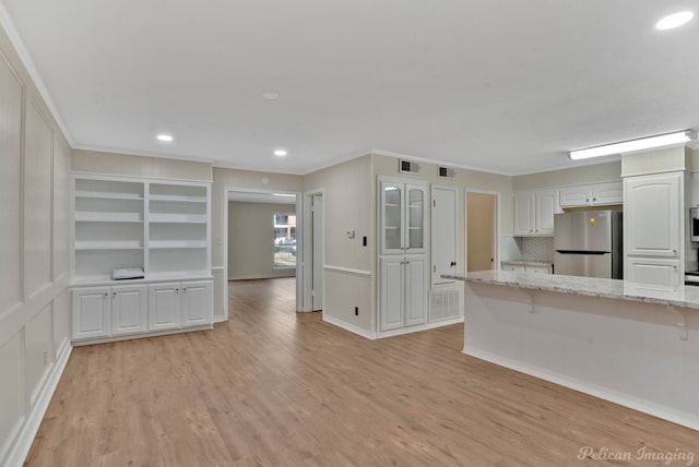 kitchen featuring white cabinetry, light stone countertops, stainless steel appliances, light wood-type flooring, and crown molding