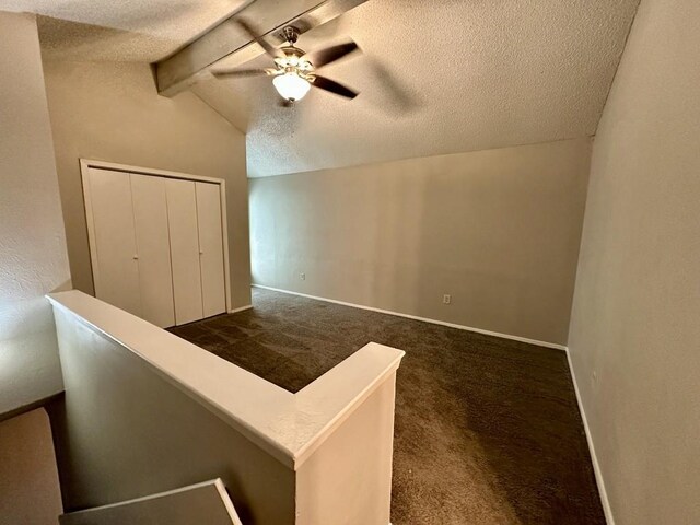 interior space with baseboards, dark carpet, a textured ceiling, and vaulted ceiling with beams