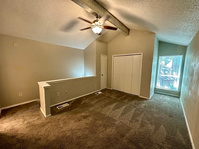 unfurnished bedroom with vaulted ceiling with beams, dark colored carpet, ceiling fan, and a textured ceiling