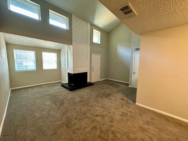 unfurnished living room with a textured ceiling, dark colored carpet, and a wealth of natural light