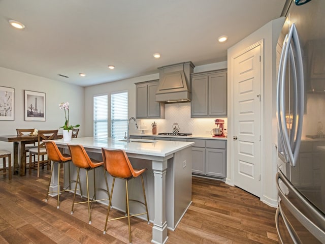 kitchen with gray cabinetry, a kitchen island with sink, stainless steel appliances, dark hardwood / wood-style floors, and custom range hood