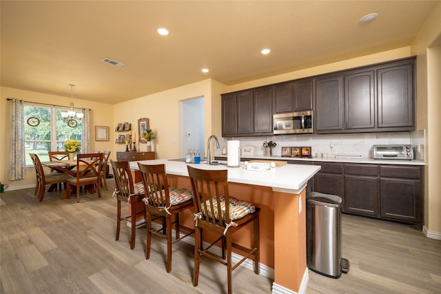 kitchen with dark brown cabinets, light wood-type flooring, an island with sink, a notable chandelier, and hanging light fixtures