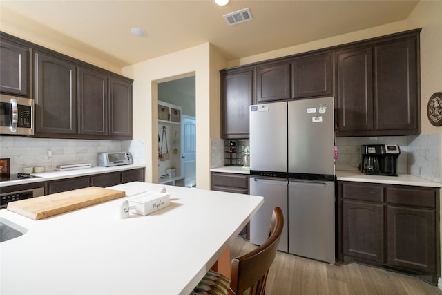 kitchen featuring light wood-type flooring, appliances with stainless steel finishes, dark brown cabinetry, and tasteful backsplash