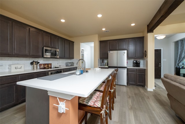 kitchen with tasteful backsplash, an island with sink, light hardwood / wood-style flooring, stainless steel appliances, and dark brown cabinetry