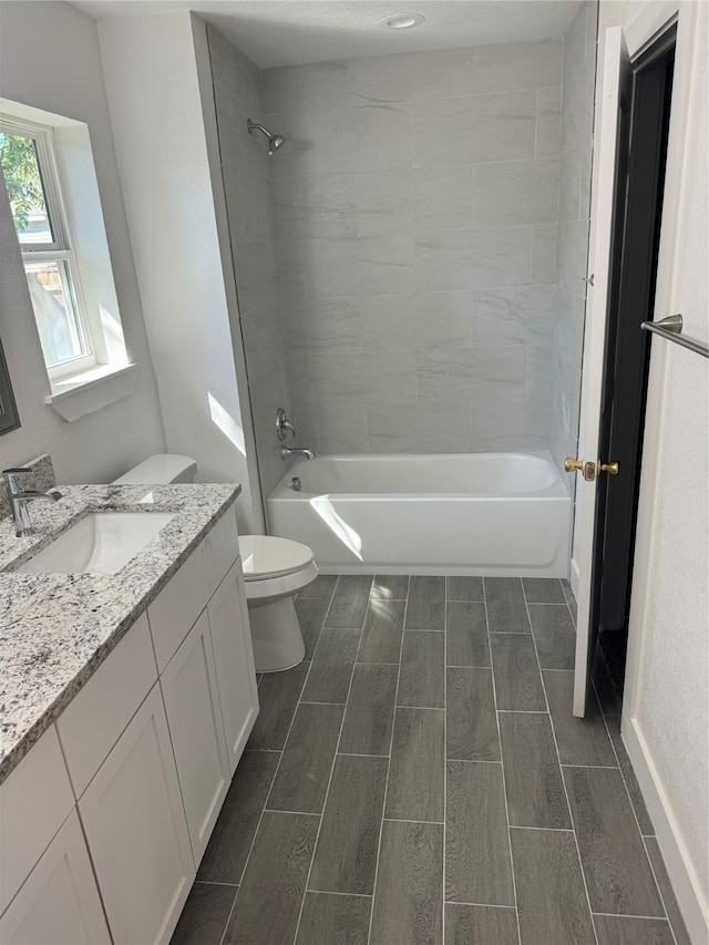 full bathroom featuring vanity, tiled shower / bath combo, and toilet