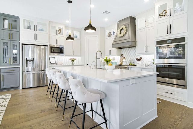 kitchen featuring a center island with sink, white cabinetry, appliances with stainless steel finishes, dark hardwood / wood-style flooring, and decorative backsplash