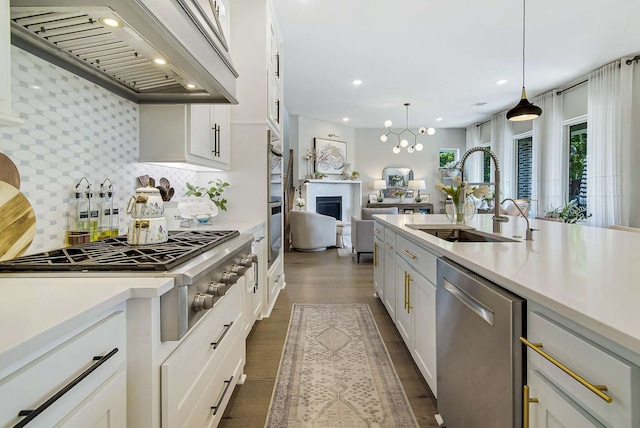 kitchen with white cabinets, sink, appliances with stainless steel finishes, decorative light fixtures, and premium range hood