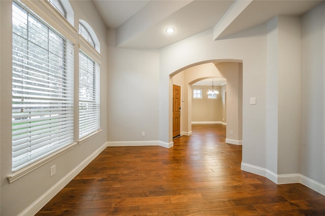 spare room with dark hardwood / wood-style floors, a wealth of natural light, and a notable chandelier