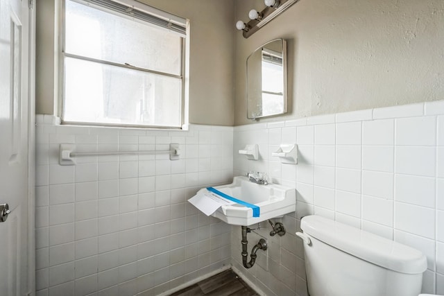 bathroom with tile walls, sink, toilet, and a healthy amount of sunlight