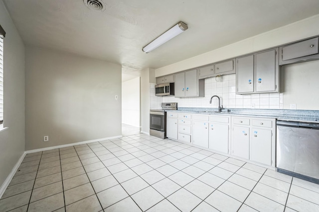 kitchen with light tile patterned flooring, sink, gray cabinetry, backsplash, and stainless steel appliances