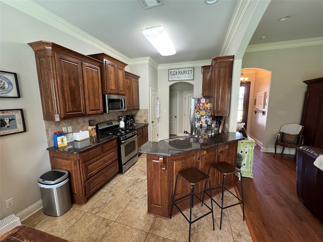 kitchen featuring ornamental molding, appliances with stainless steel finishes, light wood-type flooring, and kitchen peninsula