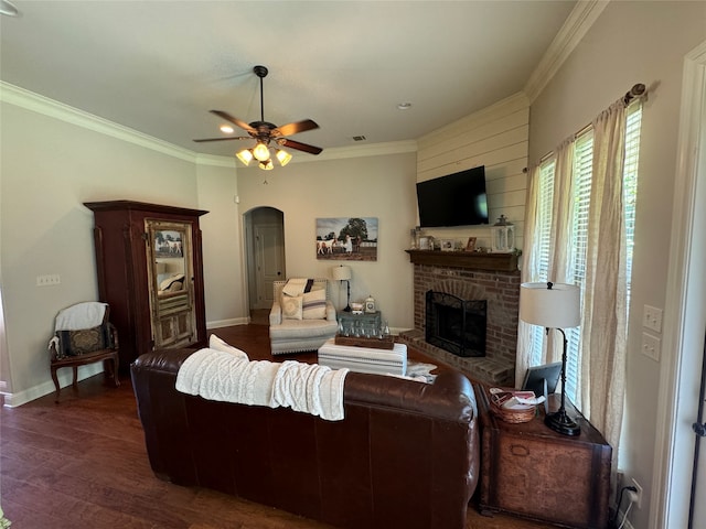 living room featuring ceiling fan, ornamental molding, a brick fireplace, and dark wood-type flooring