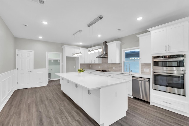 kitchen featuring a kitchen island, white cabinetry, wall chimney range hood, stainless steel appliances, and sink