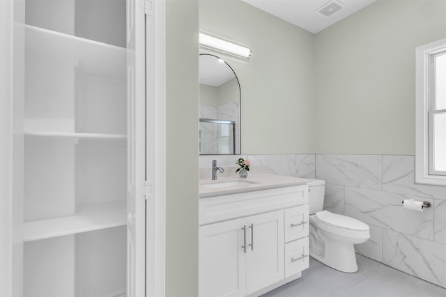 bathroom featuring toilet, a shower with door, tile walls, tile patterned floors, and vanity