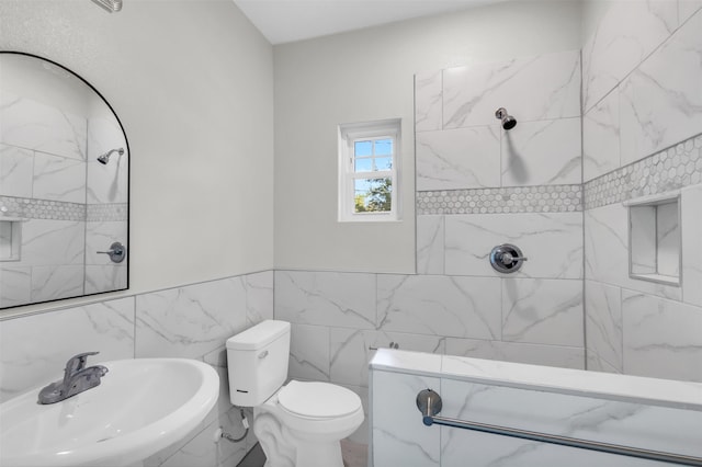 bathroom with toilet, tile walls, sink, and a tile shower