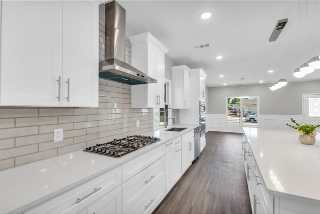 kitchen with stainless steel gas stovetop, wall chimney range hood, pendant lighting, sink, and white cabinets