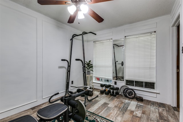 workout area with a textured ceiling, wood-type flooring, ornamental molding, and ceiling fan