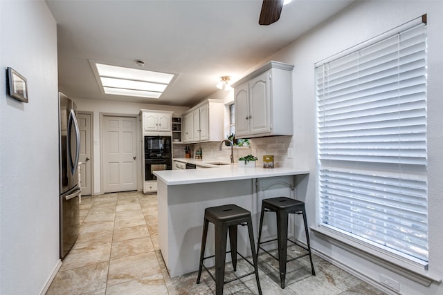 kitchen featuring black appliances, kitchen peninsula, white cabinetry, and tasteful backsplash