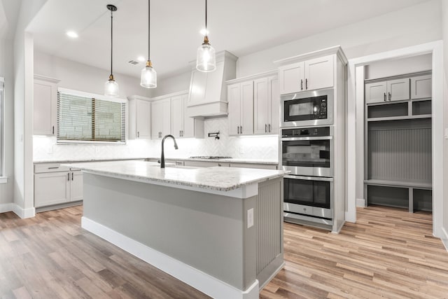 kitchen featuring sink, light stone counters, an island with sink, light hardwood / wood-style flooring, and white cabinets