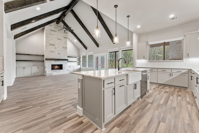 kitchen featuring a stone fireplace, stainless steel dishwasher, white cabinetry, and a center island with sink